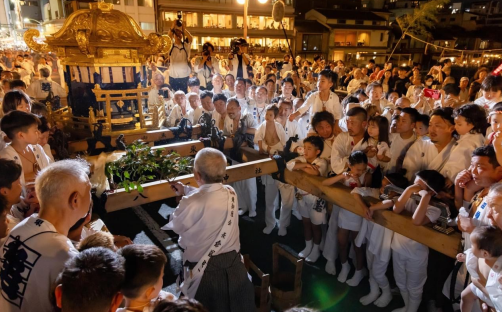 在四條大橋上會進行神事。用奉幣（ほうへい）裝飾的榊（さかき），將早上取來的「神用水」（しんようすい）灑在神輿上。在這個時候，家有孩子的父母會把孩子伸向神輿，讓水灑在孩子身上。（攝影：安田）